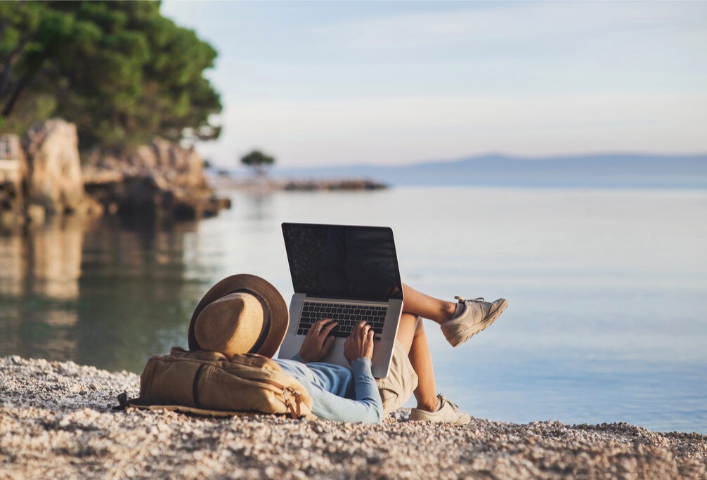 Nomada digital sentado en la playa con su laptop